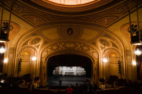 Interior of a grand theater with ornate architecture, featuring a dark stage and empty seats.