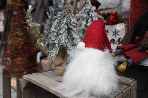 A festive display featuring a Santa figure with a red hat and fluffy white beard, surrounded by small decorated trees.