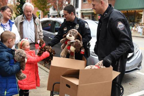 Two police officers hand out stuffed animals to children outside, while adults watch and smile nearby.