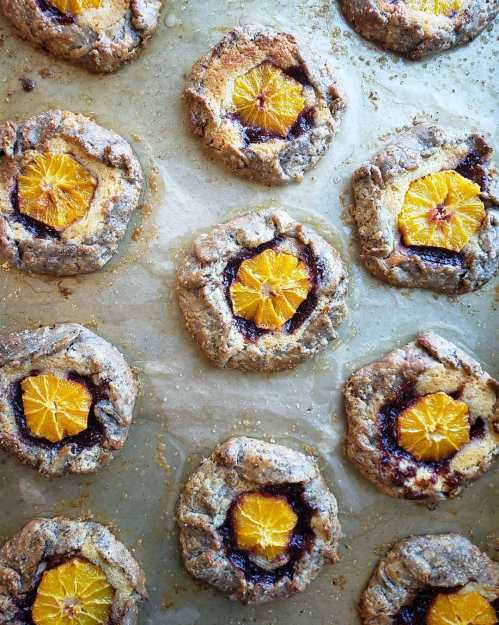 Baked cookies with a jam center and orange slices on top, arranged on parchment paper.