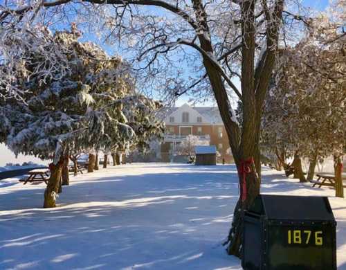 A snowy landscape with trees, a building in the background, and a black mailbox marked "1876."