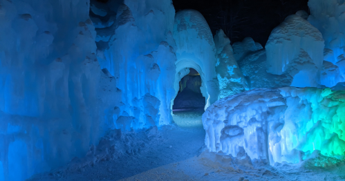 A glowing ice cave with blue and green lights illuminating the icy formations and a winding path through the snow.