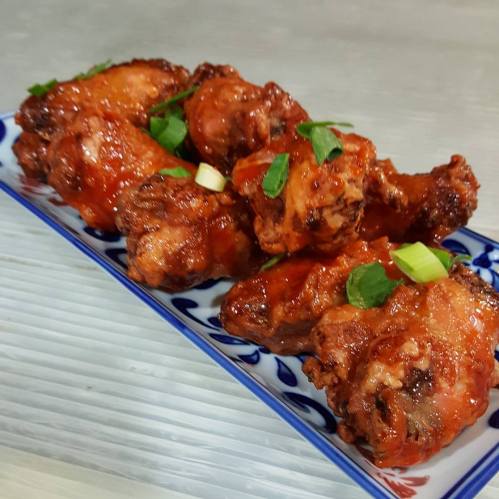 A plate of glazed chicken wings garnished with green onions, arranged neatly on a decorative blue and white dish.