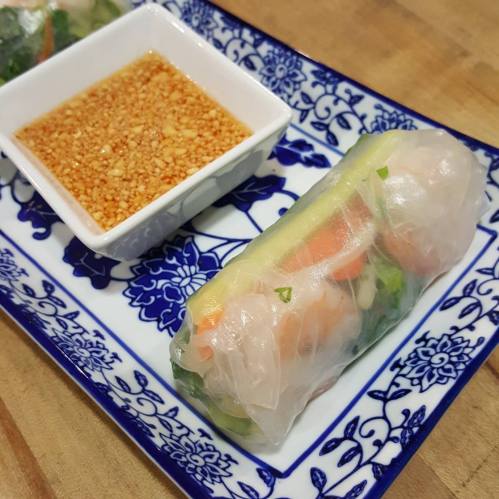 Fresh spring rolls with shrimp and vegetables, served with a side of dipping sauce on a decorative plate.