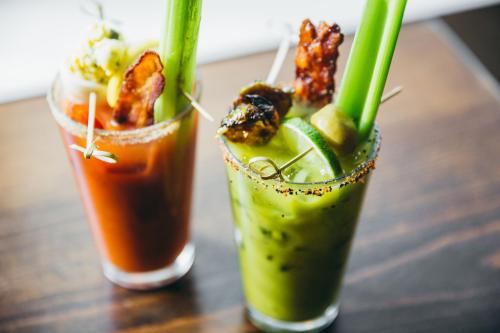 Two colorful cocktails with celery sticks, garnishes, and rimmed glasses on a wooden table.