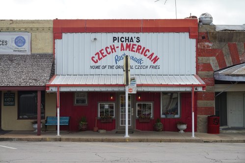A quaint restaurant with a red and white sign reading "Picha's Czech-American Restaurant" and a porch with flower pots.