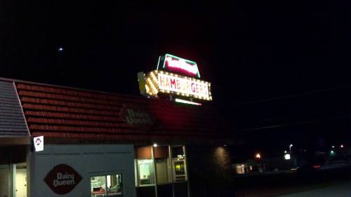 A brightly lit sign for a hamburger restaurant at night, with a Dairy Queen logo visible in the foreground.
