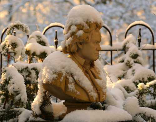 A snow-covered bust of Beethoven surrounded by greenery, with a soft winter light in the background.