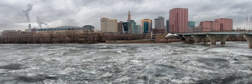 A panoramic view of a city skyline over a frozen river, with cloudy skies and buildings in the background.