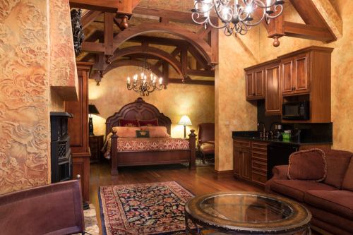 Cozy, elegantly decorated room with a wooden bed, chandelier, and a sitting area featuring a rug and coffee table.
