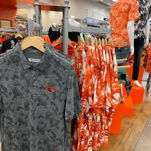 Display of colorful Hawaiian shirts and a gray polo with a logo in a retail store.