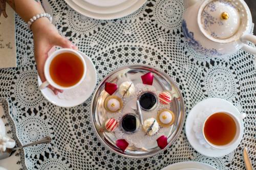 A table set with tea, pastries, and rose petals, featuring a hand holding a cup of tea.