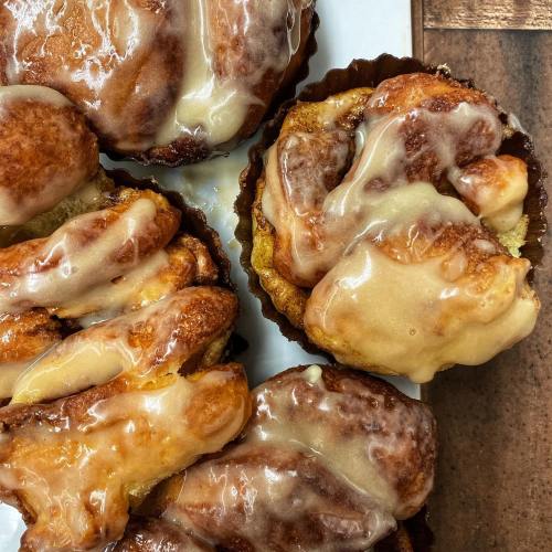 Close-up of freshly baked cinnamon rolls drizzled with creamy icing on a white plate.