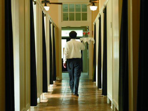 A waiter carrying a tray with drinks walks down a hallway lined with curtains.