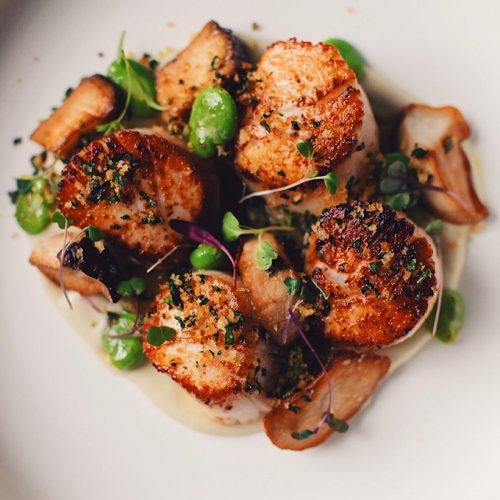 Seared scallops topped with herbs and breadcrumbs, served with green peas and mushrooms on a creamy sauce.