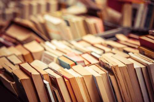 A close-up of a stack of various books with visible spines and pages, creating a colorful, textured display.