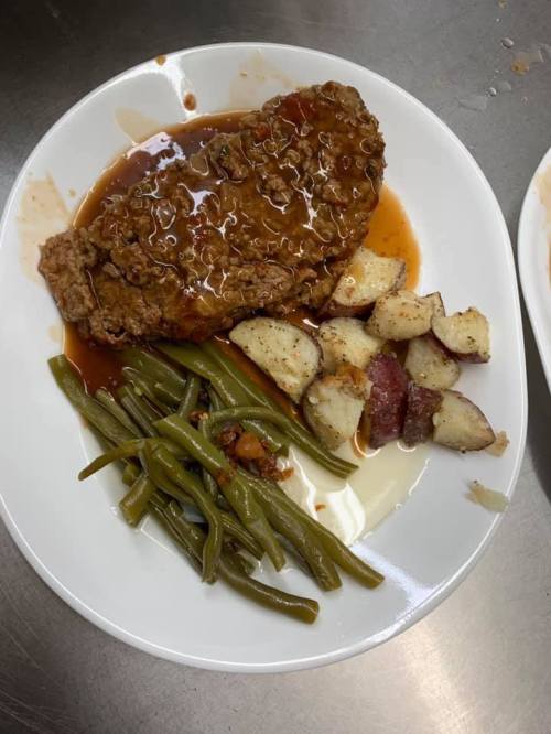 A plate of meatloaf with gravy, green beans, and roasted potatoes.