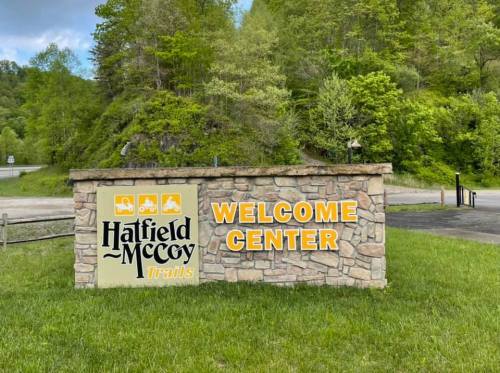 Sign for the Hatfield-McCoy Trails Welcome Center, surrounded by greenery and trees.