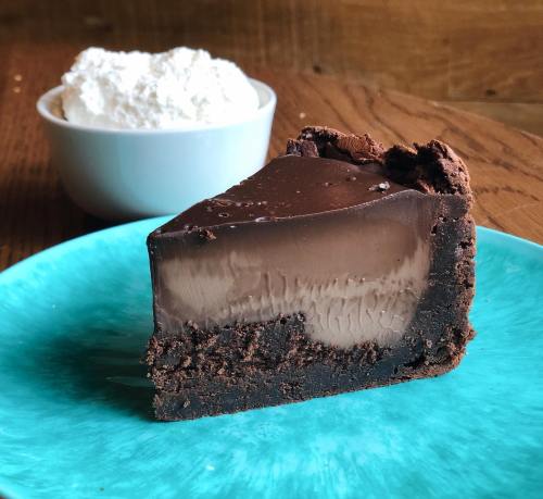 A slice of rich chocolate pie on a turquoise plate, with a bowl of whipped cream in the background.