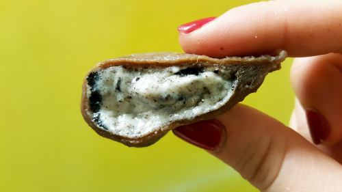 A hand holding a half of a chocolate treat, revealing a creamy filling with dark cookie bits inside.