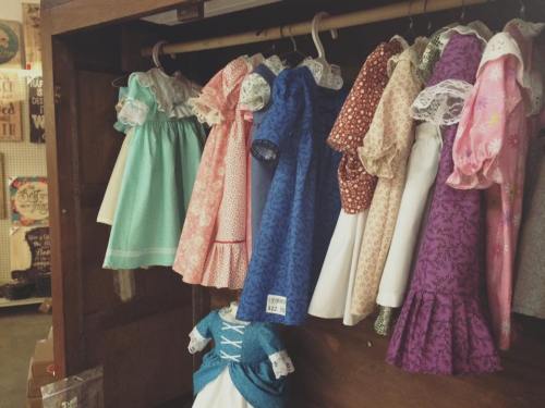 A display of colorful children's dresses hanging on a wooden rack, featuring various patterns and styles.