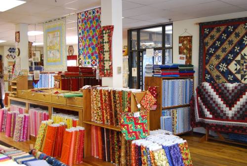 A colorful fabric store filled with rolls of fabric, quilts on display, and vibrant patterns throughout the space.