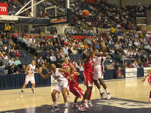 A basketball game in progress, with players from both teams competing for the ball in a packed arena.