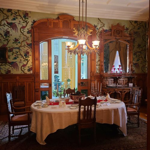 Elegant dining room with a round table set for a meal, surrounded by ornate wooden furniture and floral wallpaper.