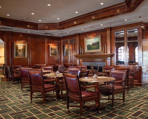 Cozy restaurant interior with wooden paneling, tables, and chairs, featuring artwork and soft lighting.