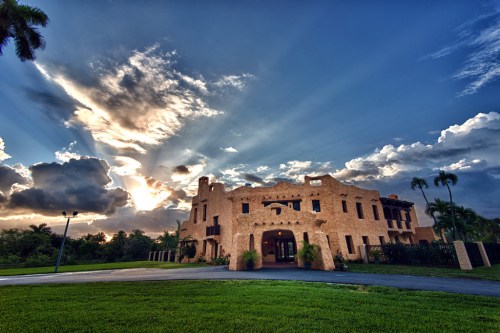 A large, ornate building with a textured facade, set against a dramatic sky with rays of sunlight breaking through clouds.