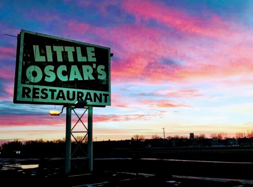 Sign for Little Oscar's Restaurant against a colorful sunset sky.