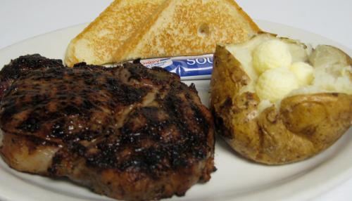 A plate with grilled steak, a baked potato with butter, toasted bread, and a packet of sour cream.