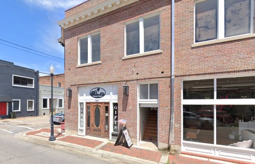 A brick building with a sign for "Gifts" and stairs leading up, located on a quiet street.