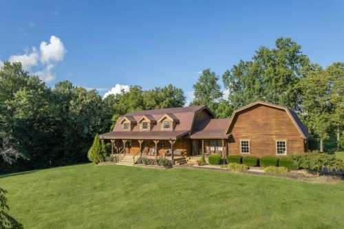A large wooden house surrounded by greenery and trees under a clear blue sky.