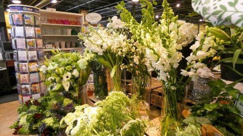A vibrant display of various flowers and greenery in a floral shop, showcasing tall arrangements and lush plants.