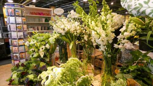 A vibrant display of various flowers and greenery in a floral shop, showcasing tall arrangements and lush plants.