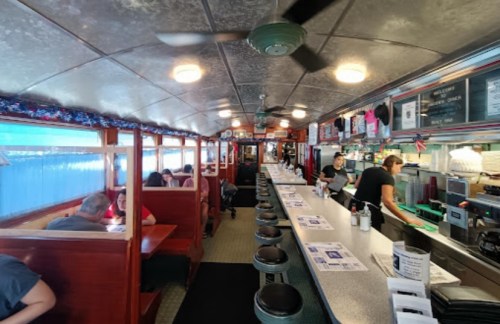Interior of a diner with booths and a long counter, featuring patrons and staff in a cozy, retro atmosphere.
