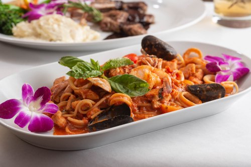 A plate of seafood pasta with shrimp, mussels, and herbs, garnished with purple orchids.
