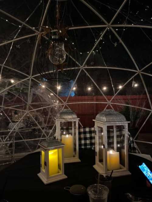 Cozy outdoor dining igloo with lanterns, candles, and string lights, creating a warm ambiance at night.