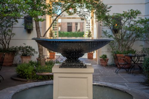 A decorative fountain with water gently cascading, surrounded by greenery and potted plants in a serene courtyard.