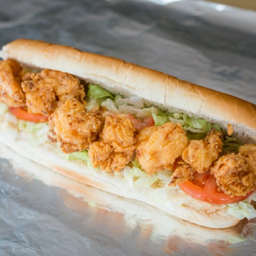A sub sandwich filled with crispy fried chicken, lettuce, and tomato on a soft hoagie roll, resting on foil.