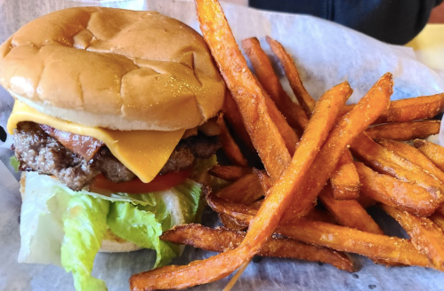 A cheeseburger with lettuce, tomato, and bacon, served with a side of crispy sweet potato fries.