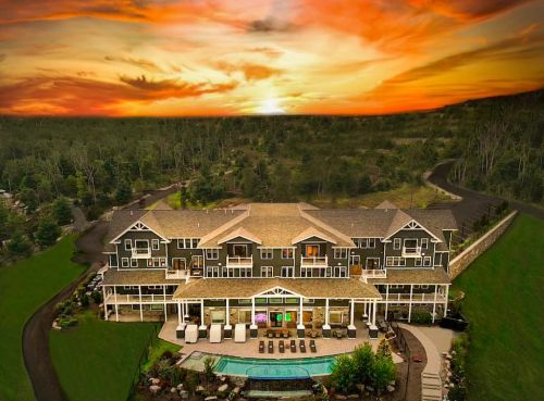 A large, modern house with a pool, surrounded by greenery, under a vibrant sunset sky.