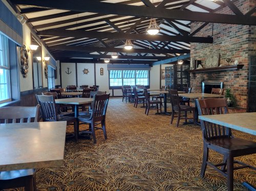 A spacious dining area with wooden tables and chairs, featuring a rustic ceiling and a brick fireplace.