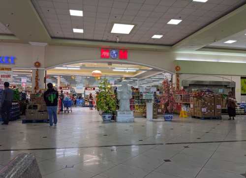 A grocery store interior with colorful displays, shopping carts, and a statue in the center under bright lights.