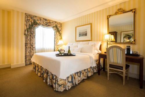 Cozy hotel room with a king bed, elegant decor, a desk, and large windows with soft curtains.