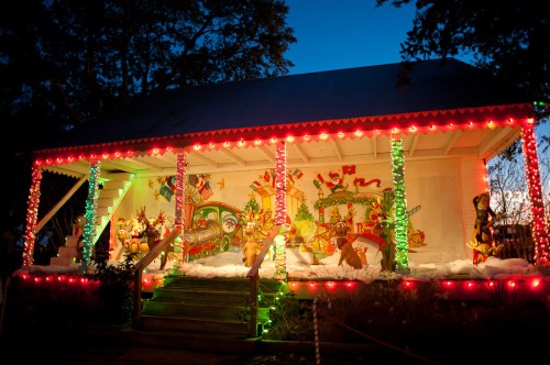 A festive house decorated with colorful lights and holiday-themed murals, set against a twilight sky.