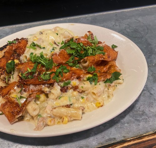 A plate of creamy pasta topped with crispy fried pieces and fresh herbs, served on a rustic surface.