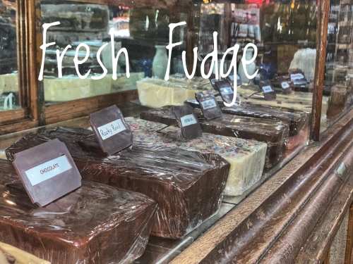 A display of various wrapped fudge blocks in a shop window, labeled with flavors. Text reads "Fresh Fudge."