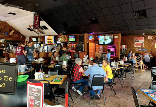 A busy restaurant interior with patrons dining, colorful decor, and multiple TVs showing sports.